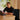 Person using a laptop at a desk with a plant and curtain in the background