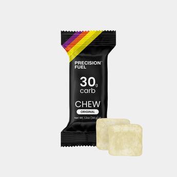 A single Precision Fuel Chew supplement bar in its black wrapper, shown next to two unwrapped pale yellow chewable tablets on a light gray background.