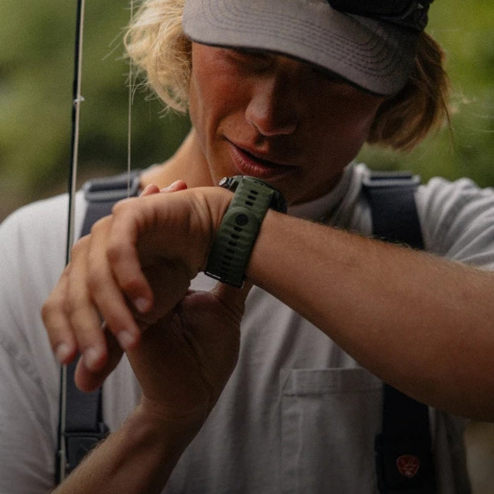 Person outdoors wearing a white cap and light-colored shirt, looking at their green watch.