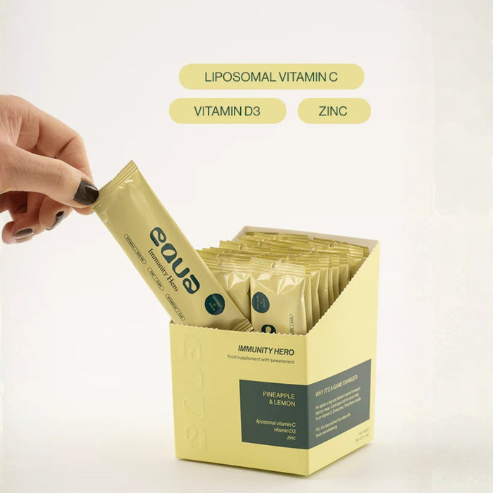 Hand holding a eava supplement packet above a display box of eava immune support packets on a white background.