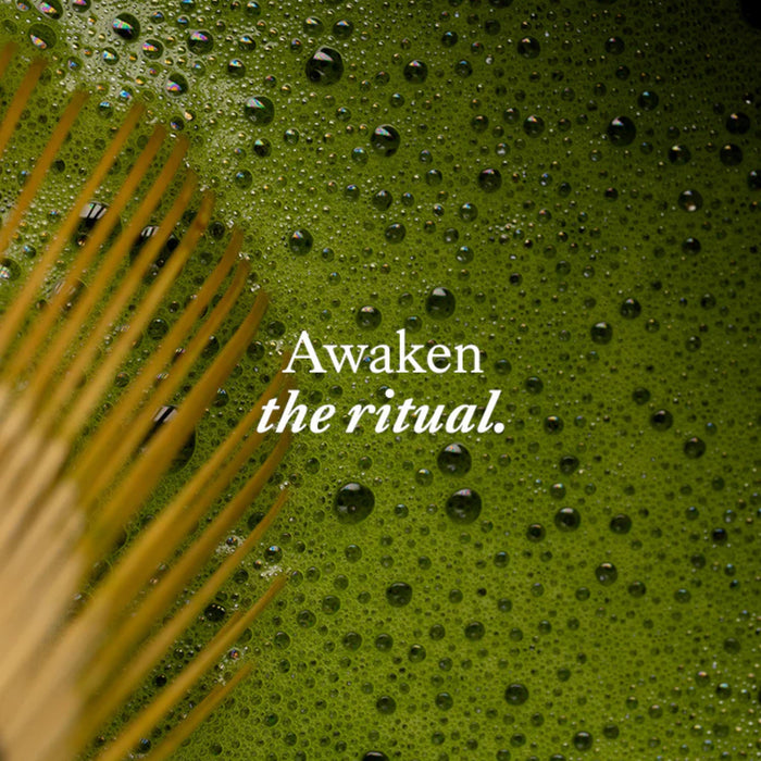 Text 'Awaken the ritual.' on a green background with water droplets and a plant leaf.