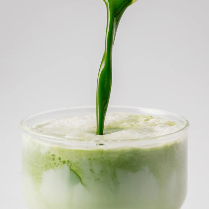 Green liquid being poured into a glass with ice on a light gray background