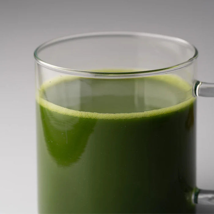 Clear glass mug filled with green liquid on a gray background