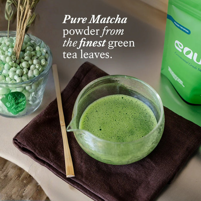 Matcha green tea powder in a glass bowl with packaging and text on a wooden surface.