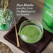 Matcha green tea powder in a glass bowl with packaging and text on a wooden surface.