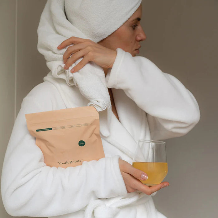 Person in a white robe with a towel on their head, holding a glass of orange juice and a package.