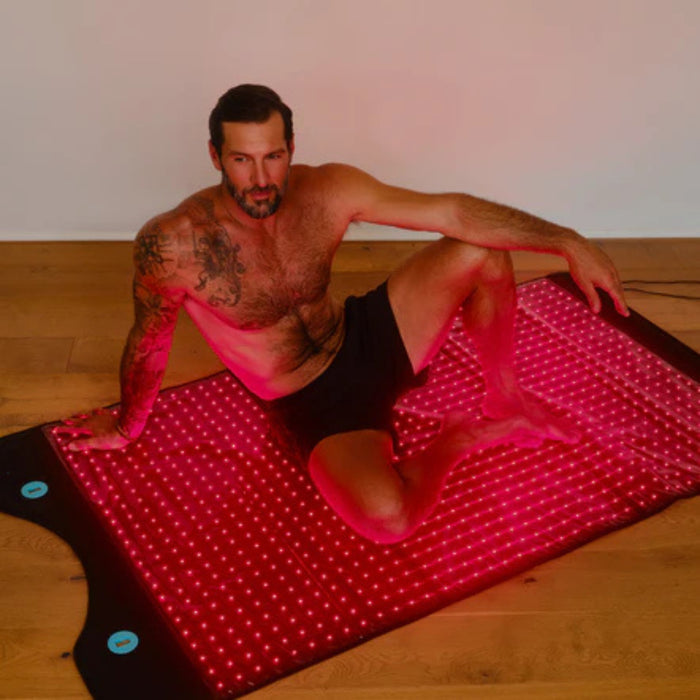 Man sitting on a red LED mat in a room with wooden floor and white walls