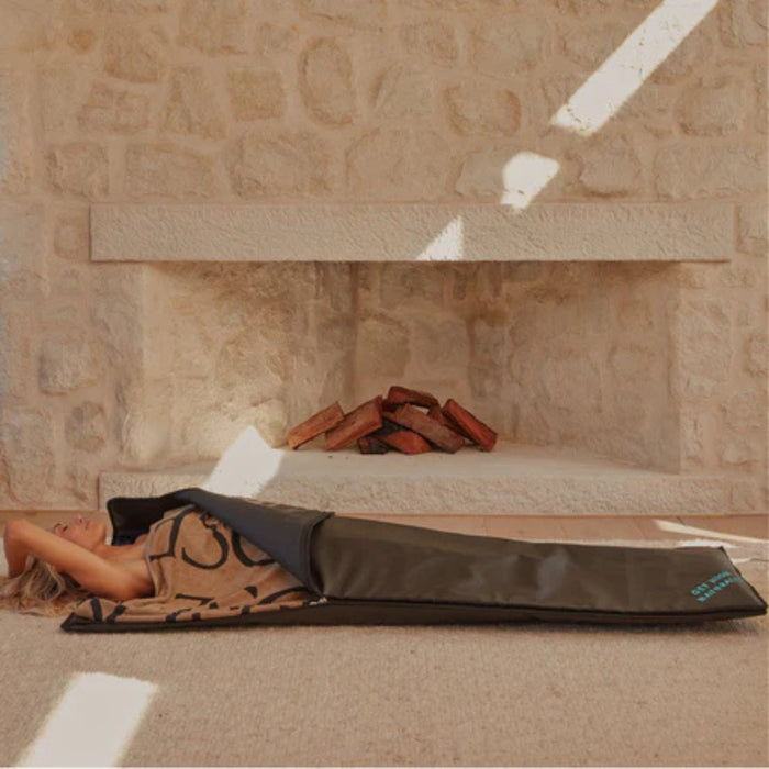 Person lying on a brown mat against a stone wall.