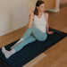 Woman practicing yoga on a mat with a wooden floor and white wall background