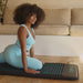 Woman using a black and blue mat on a wooden floor with a beige couch in the background.