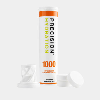 A white cylindrical tube of Precision Hydration 1000 effervescent electrolyte tablets stands upright on a light gray background, with its white cap removed and placed beside it.