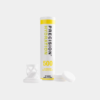 A white cylindrical Precision Hydration 500 electrolyte salt tube with yellow accents, shown on a light gray background with white caps and a small white container in front.