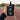 A hand holding a black Precision Fuel 90g carb gel pouch on a blurred running track at sunset.
