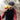 A man wearing a black cycling helmet and a black and red cycling jersey drinks from a bright yellow bottle outdoors.