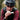 A close-up lifestyle shot of a cyclist wearing a black helmet and a black and burgundy jersey, eating a protein bar in an outdoor forest setting.