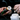 A close-up lifestyle shot of a person's hands pouring a white tablet from a black and orange tube into a clear plastic bottle. The person is wearing a silver ring on their left hand, and the background is a dark, blurred interior.