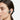 A close-up side profile of a woman wearing a dark gray behind-the-ear wireless earbud in her ear. Light blue graphic wave and arrow overlays illustrate sound and earbud movement, set against a clean white background.