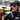 A close-up lifestyle shot of a cyclist wearing a black SIS helmet and cycling jersey drinking from a white SIS water bottle. The cyclist is wearing reflective gold-tinted sunglasses and a black helmet.